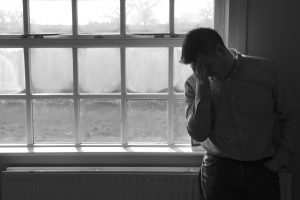 Lone anonymous middle aged man suffering depression or anxiety. Â Looking sad, worried, frustrated, in pain or desperate with hands on head leaning against an empty white wall.